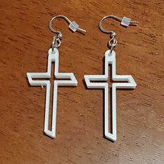 two silver cross shaped earrings sitting on top of a wooden table