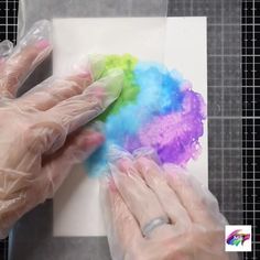 two hands in white gloves are painting with colored powder on a piece of paper that is wrapped in plastic