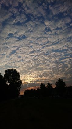 the sun is setting behind some clouds in the sky with trees on either side of it