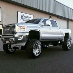 a silver truck is parked in front of a building with large tires and rims