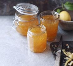 three jars filled with honey sitting on top of a table next to a cutting board