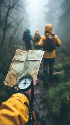 a person holding a compass and looking at it in the foggy forest with other people