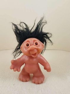 a troll doll with long black hair on it's head sitting on a white surface