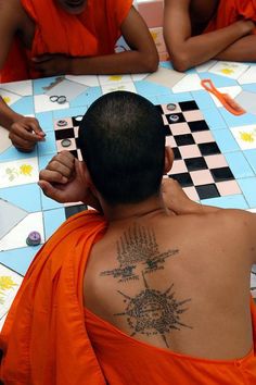 a man with tattoos on his back sitting in front of other men at a table