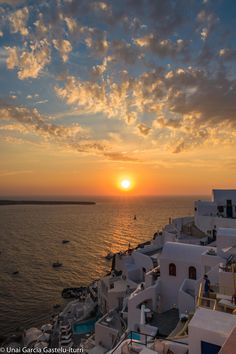 the sun is setting over an ocean with white buildings and boats in the water below