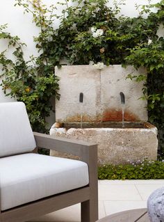 an outdoor fountain surrounded by greenery in the middle of a patio with two chairs