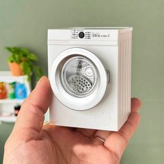 a hand holding a white washing machine in front of a green wall