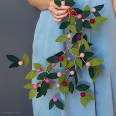 a woman in a blue dress holding a branch with pink berries and green leaves on it