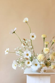 a vase filled with white and yellow flowers on top of a table next to a wall