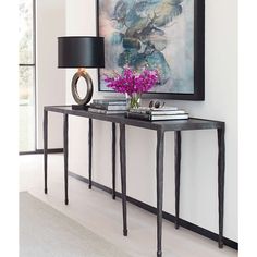 a black console table with purple flowers on top and a painting above it in a living room