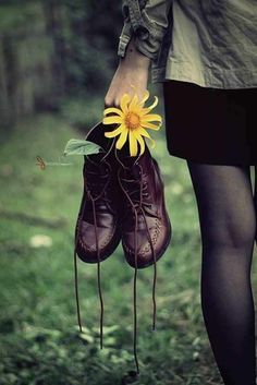 a person holding a pair of brown shoes with a yellow flower attached to them