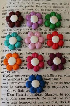 six different colored flower shaped buttons on top of an open book with french text in the background