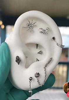 a person wearing green gloves holding up a fake ear with piercings attached to it