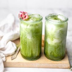 two jars filled with green liquid sitting on top of a cutting board next to a white towel