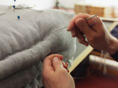 someone is stitching something on the back of a couch with pins and needles in their hands