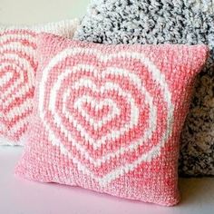 two pink and white pillows sitting next to each other on a table with knitted blankets