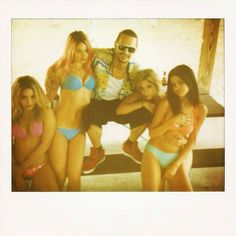 a group of young people in bikinis posing for a photo with one man holding a beer