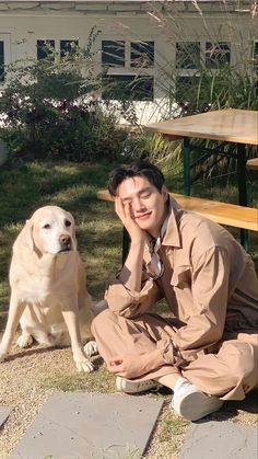 a man sitting on the ground next to a dog with his head near his face