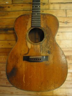 an old acoustic guitar is hanging on the wall in front of a wood paneled wall