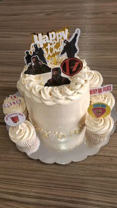 a birthday cake decorated with cupcakes and stickers on a wooden table top