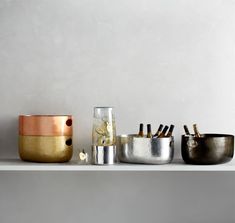 three metal containers sitting on top of a white shelf next to bottles and cups with gold rims