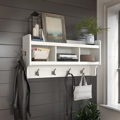 a white shelf with hooks and two coats hanging on it next to a potted plant