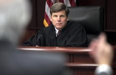 a judge sitting at a desk in front of an american flag