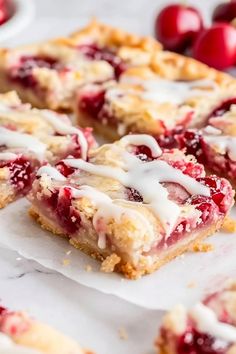 cranberry bars with icing sitting on top of white paper next to cherries