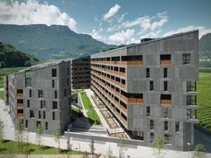 an aerial view of a large building in the middle of a green field with mountains in the background