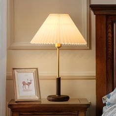 a lamp on a night stand next to a bed with a framed photo and an antelope