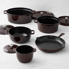 an assortment of black pots and pans on a white counter top with one pot in the middle