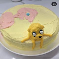 a yellow cake with pink frosting and an odd looking figure on the top, sitting on a white plate