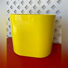 a yellow plastic pot sitting on top of a red table next to a white wall