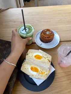 a person is sitting at a table with two sandwiches and an egg sandwich on it