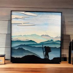 a painting is displayed on a shelf in front of a wooden wall with a mountain scene