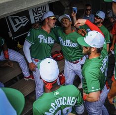 a group of baseball players in green and white uniforms talking to each other at a dugout