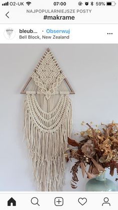 a white wall hanging next to a vase with dried flowers in it and an image of a macrame on the wall