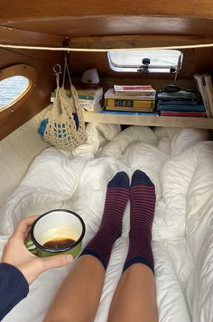 a person laying in bed with their feet up on the pillow and holding a coffee cup