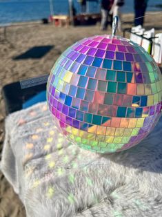 a colorful disco ball sitting on top of a table next to the ocean with people in the background