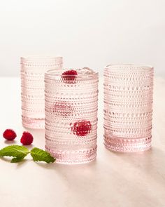 three pink glass vases sitting next to each other on a white surface with raspberries