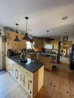 a large kitchen with an island in the middle and wooden floors on one side, two pendant lights hanging from the ceiling