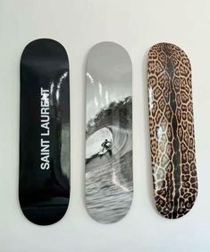 three skateboards with designs on them are lined up against a white wall, one is black and the other is leopard print