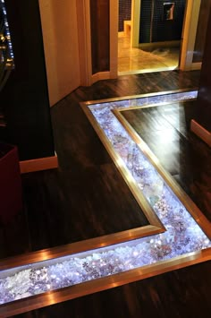 an illuminated walkway in the middle of a room with wood floors and dark colored walls