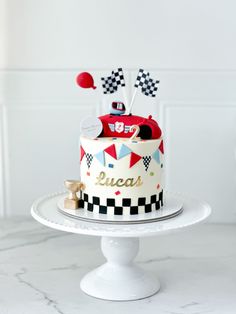 a birthday cake decorated with race cars and flags on a white pedestal in front of a wall