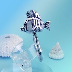 a silver fish figurine sitting on top of a glass bowl next to sea shells