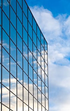 the side of a tall building with many windows and clouds in the sky behind it