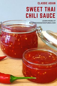 two glass jars filled with red chili sauce on top of a wooden table next to a green pepper