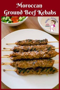 three skewered meats sitting on top of a white plate next to a bowl of salad