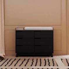 a black dresser sitting in front of a window next to a white rug and beige wall