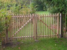 a wooden gate in the middle of a grassy area with trees and bushes behind it